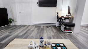 Een kamer met een houten tafel, een aan de muur bevestigde televisie en een bureau met een computer en stoel.