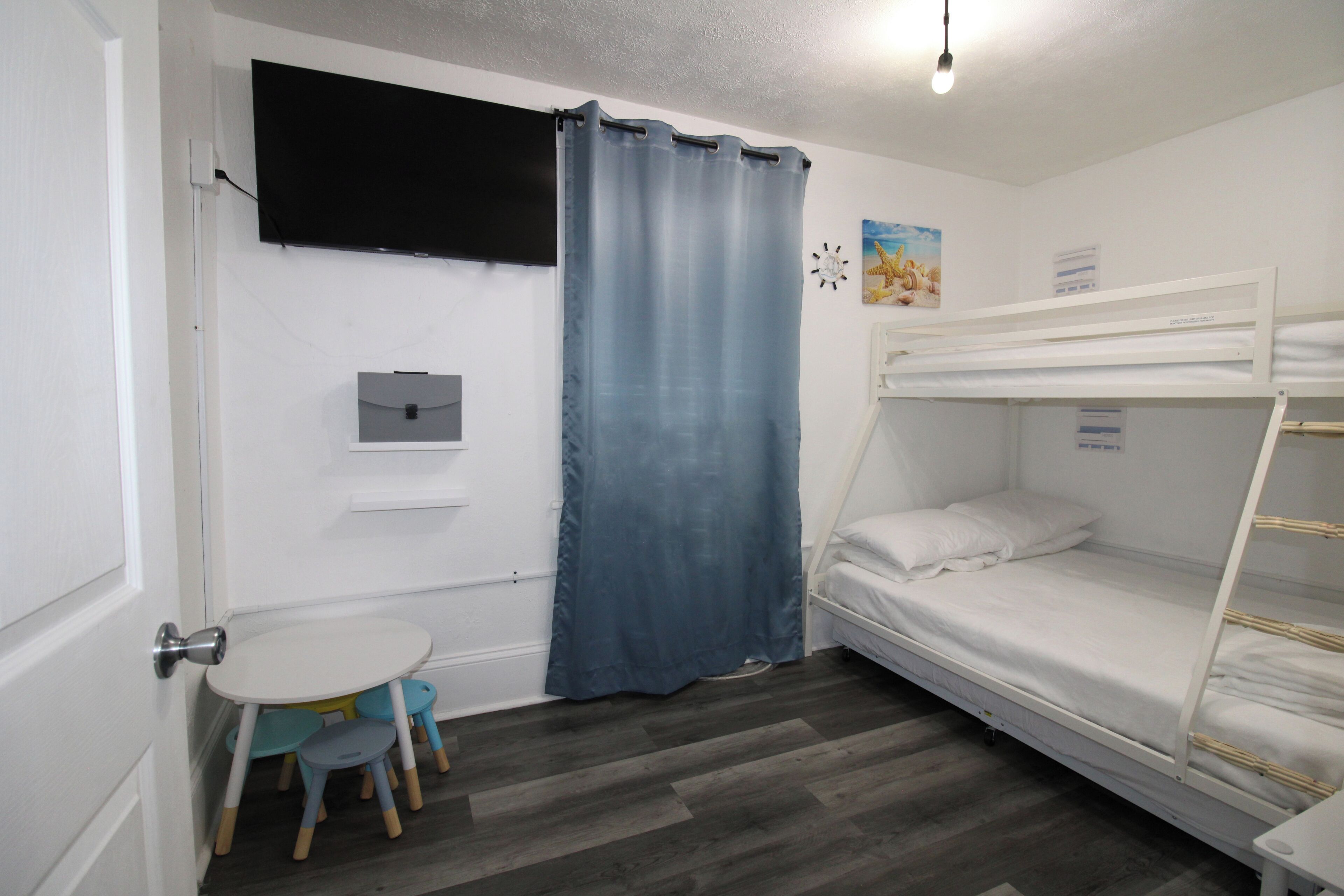 Una habitación con una cama litera, una pequeña mesa con sillas, un televisor y una cortina.