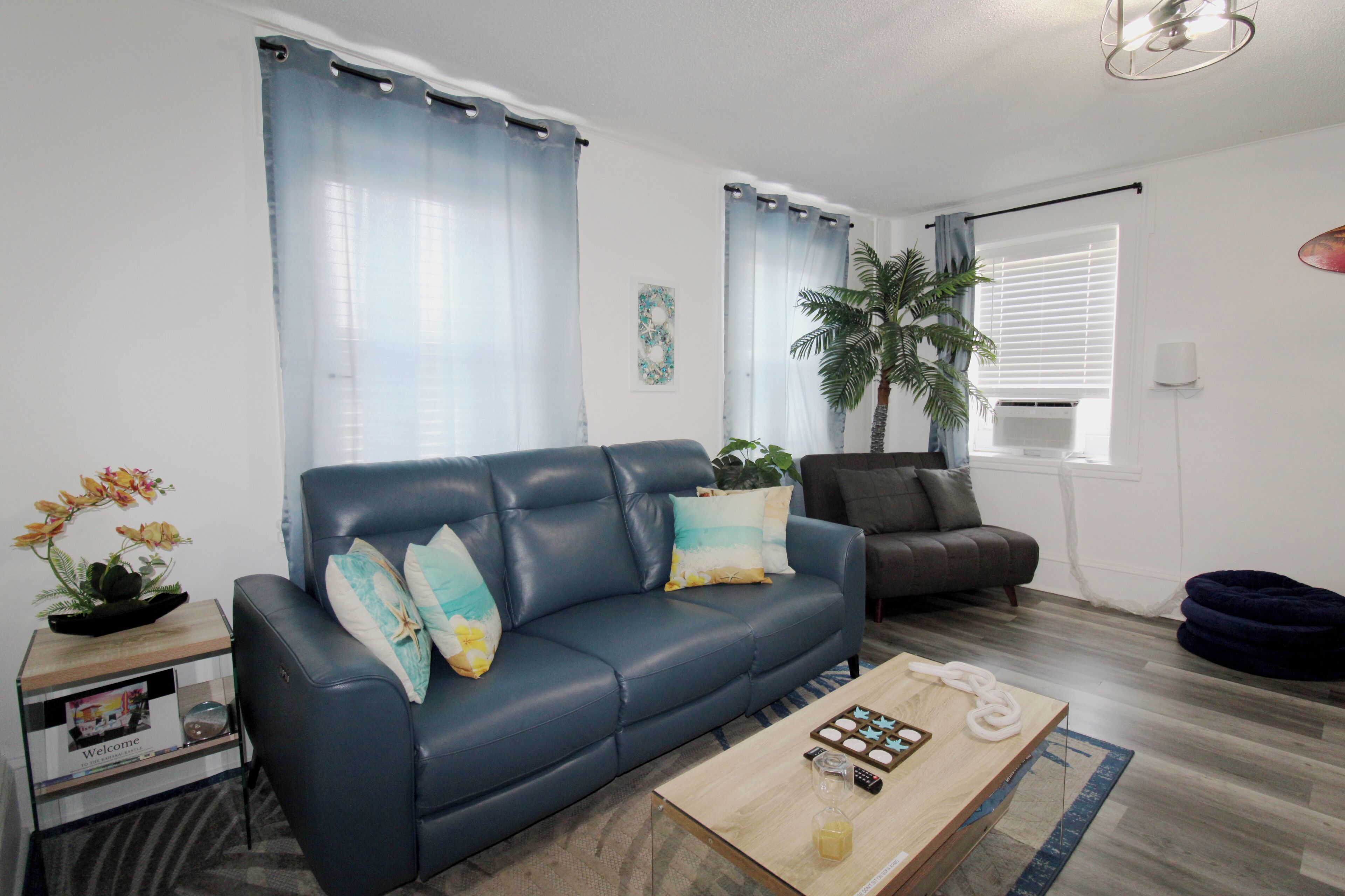 A living room with a blue sofa, a coffee table, a small side table with a plant, and a dark-colored chair.