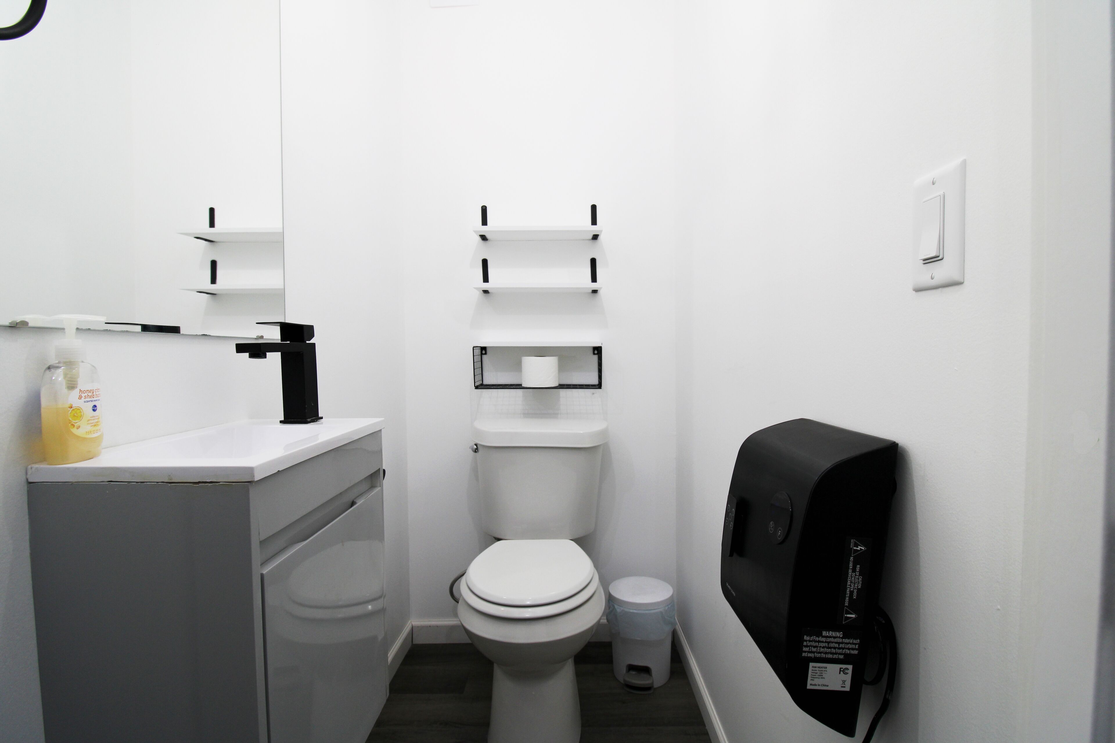 Un baño pequeño y limpio con inodoro, lavamanos y dispensador de jabón.