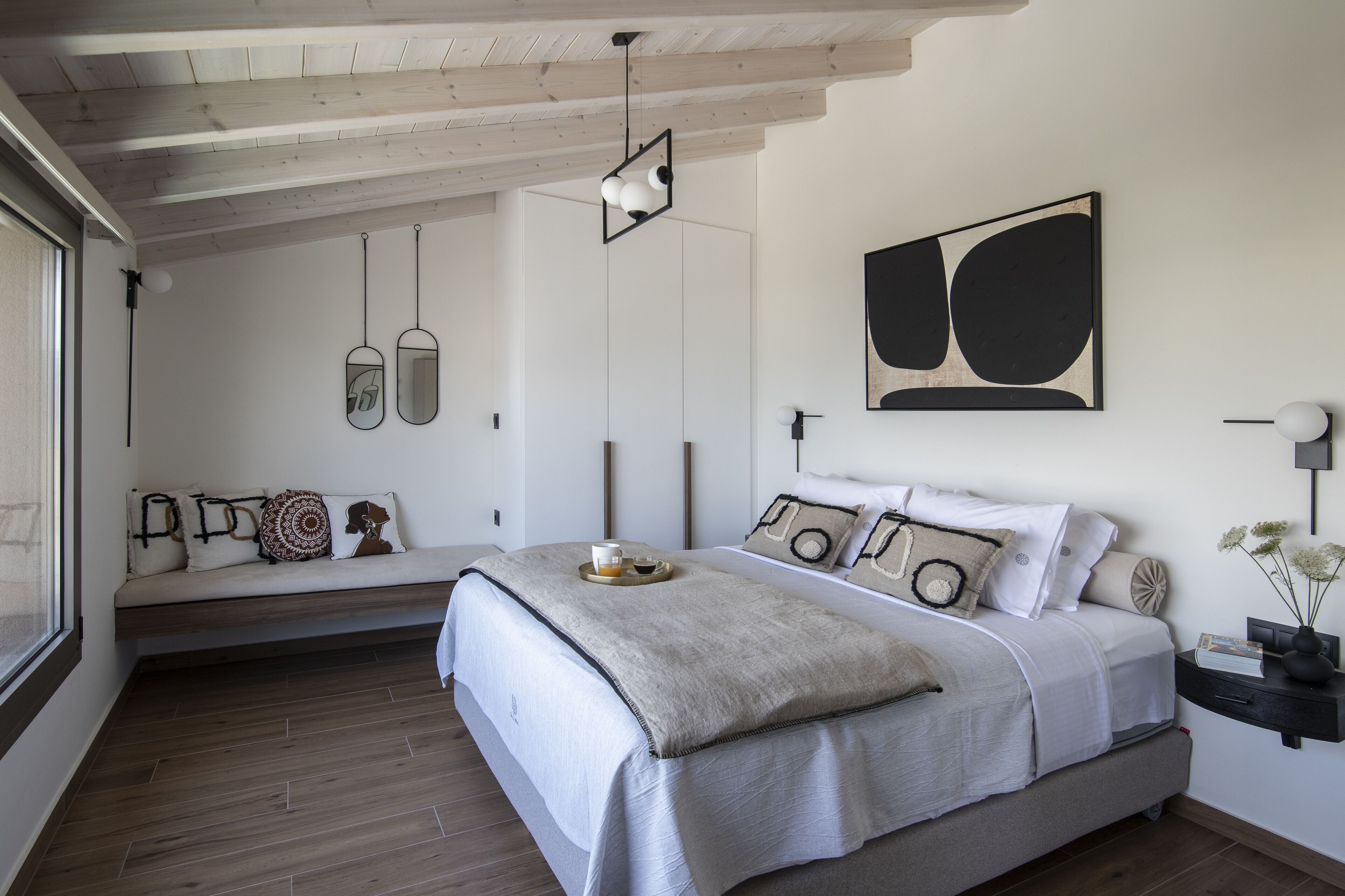 A modern bedroom with a large bed, a bench with cushions, and a wall-mounted abstract painting.