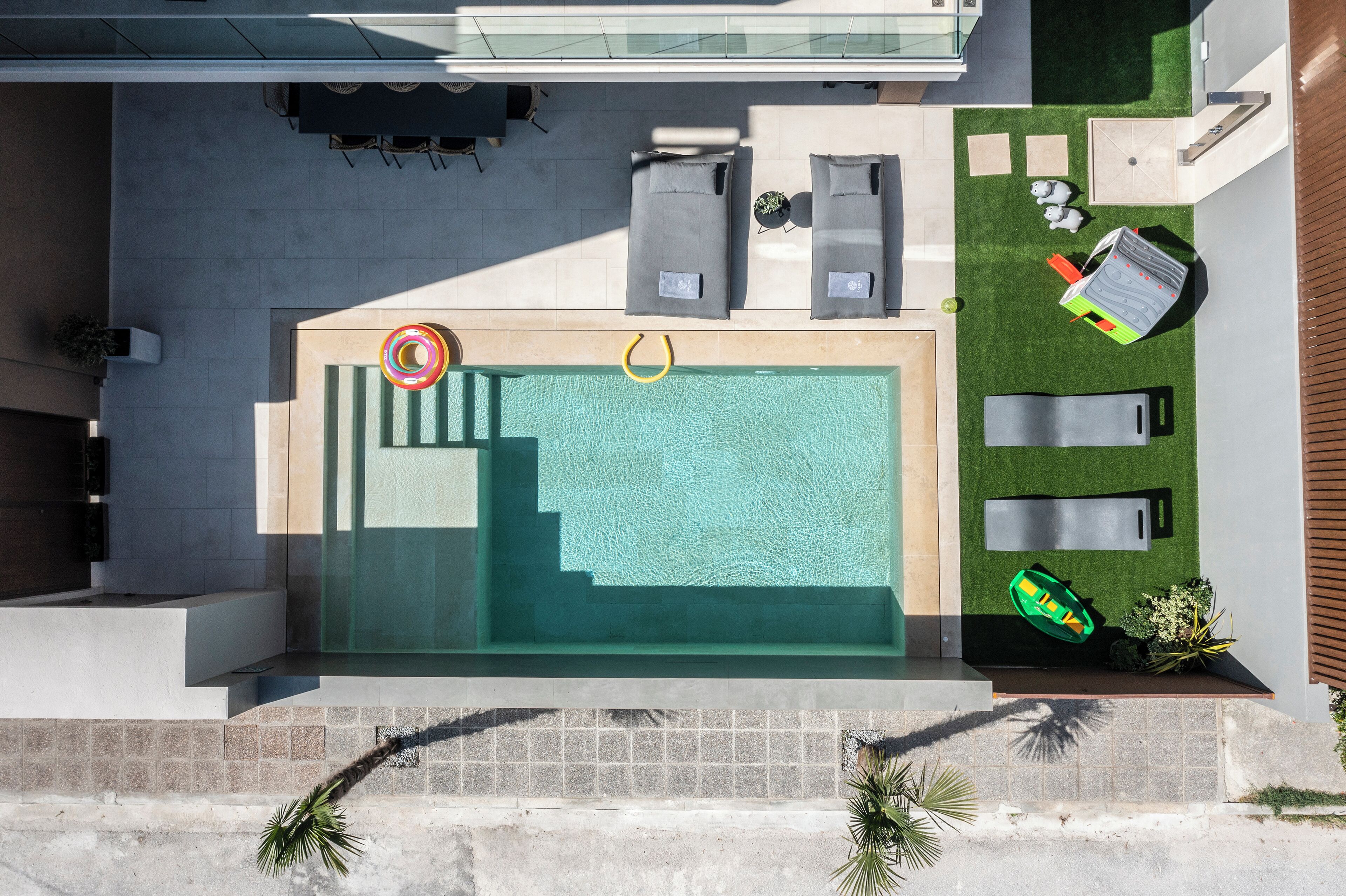 An aerial view of a modern swimming pool area with lounge chairs, a small table, and a poolside bar.