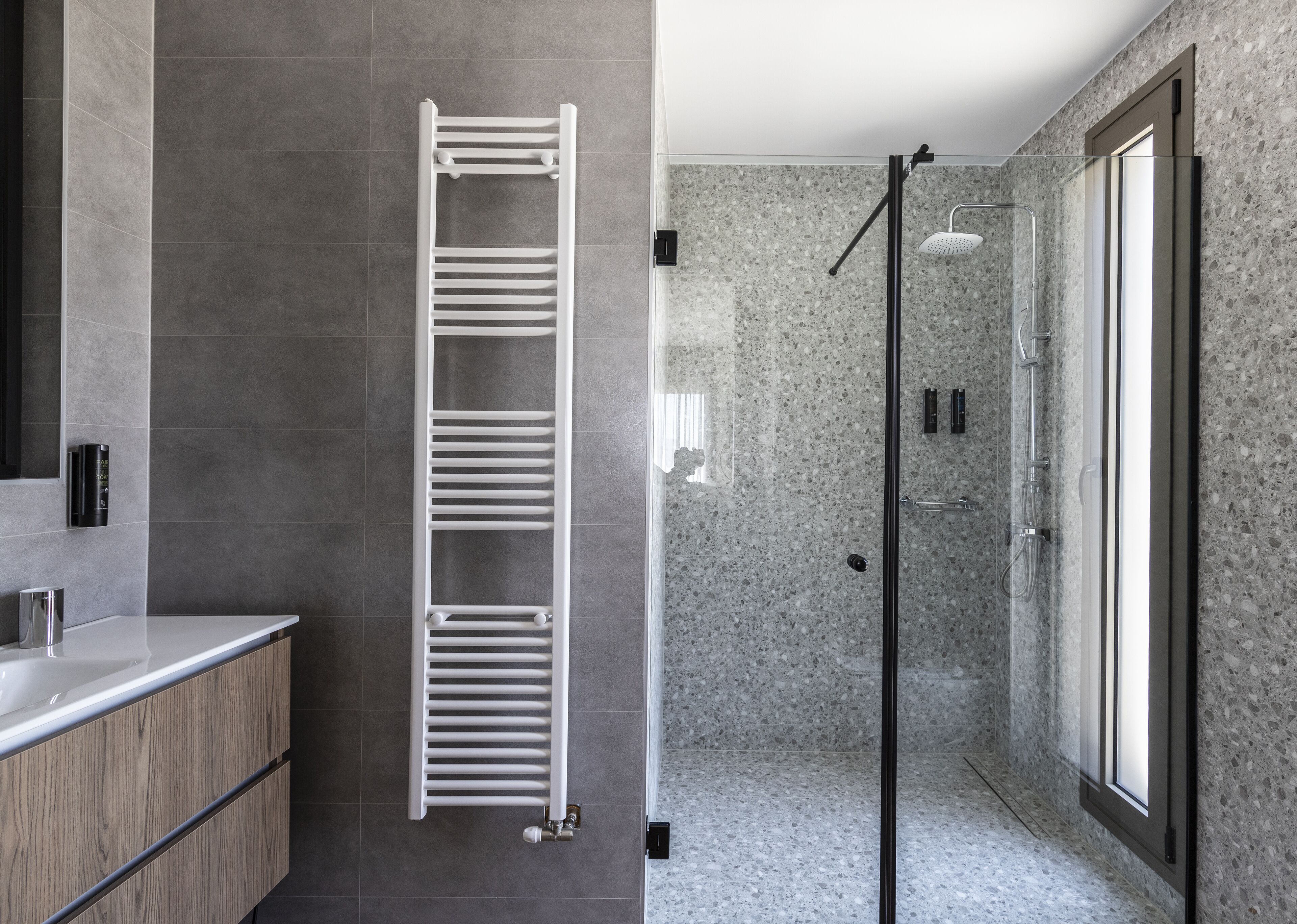 Un baño moderno con toallero empotrado, cabina de ducha de vidrio y pared de ducha con azulejos de granito.