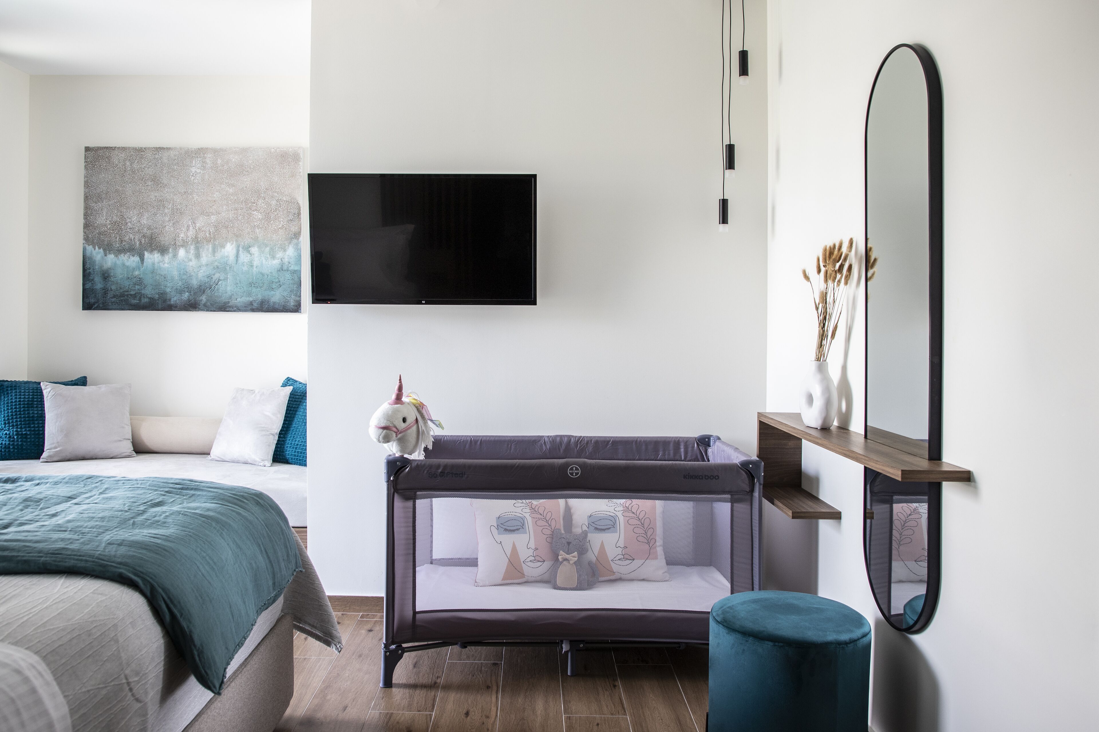 Un dormitorio moderno con una cama, una cuna para bebé, un televisor y un espejo.