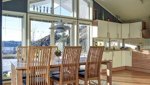 Un espace repas comprenant une table et des chaises, de grandes fenêtres et une vue sur l’extérieur.