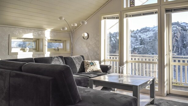 Un salon confortable avec un canapé, une table basse et un téléviseur. De grandes fenêtres offrent une vue sur un paysage enneigé.