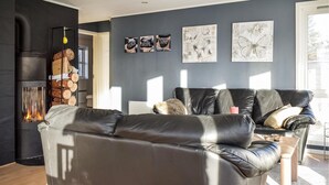 Un salon moderne avec un canapé en cuir noir, une cheminée avec des bûches et trois œuvres d’art murales portant les mots « PAIX », « ESPOIR » et « AMOUR ».