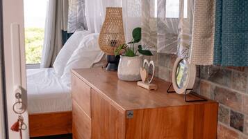 A bedroom with a wooden dresser, a wicker lamp, a potted plant, a decorative heart-shaped object, and a mirror on the dresser.