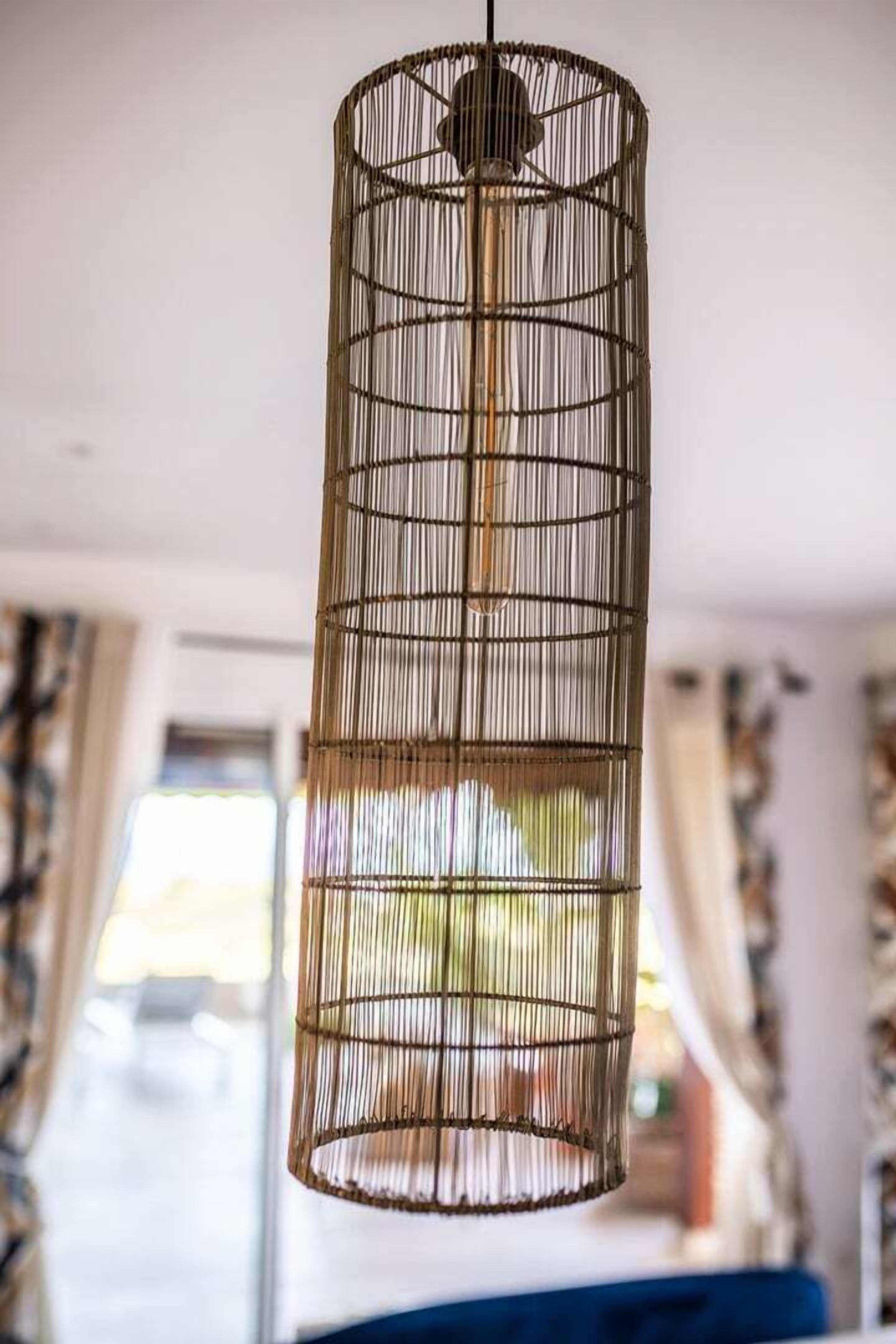 Een hanglamp van bamboe in een kamer met een bed en gordijnen.