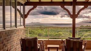 A covered outdoor seating area with a view of a mountainous landscape and a body of water.