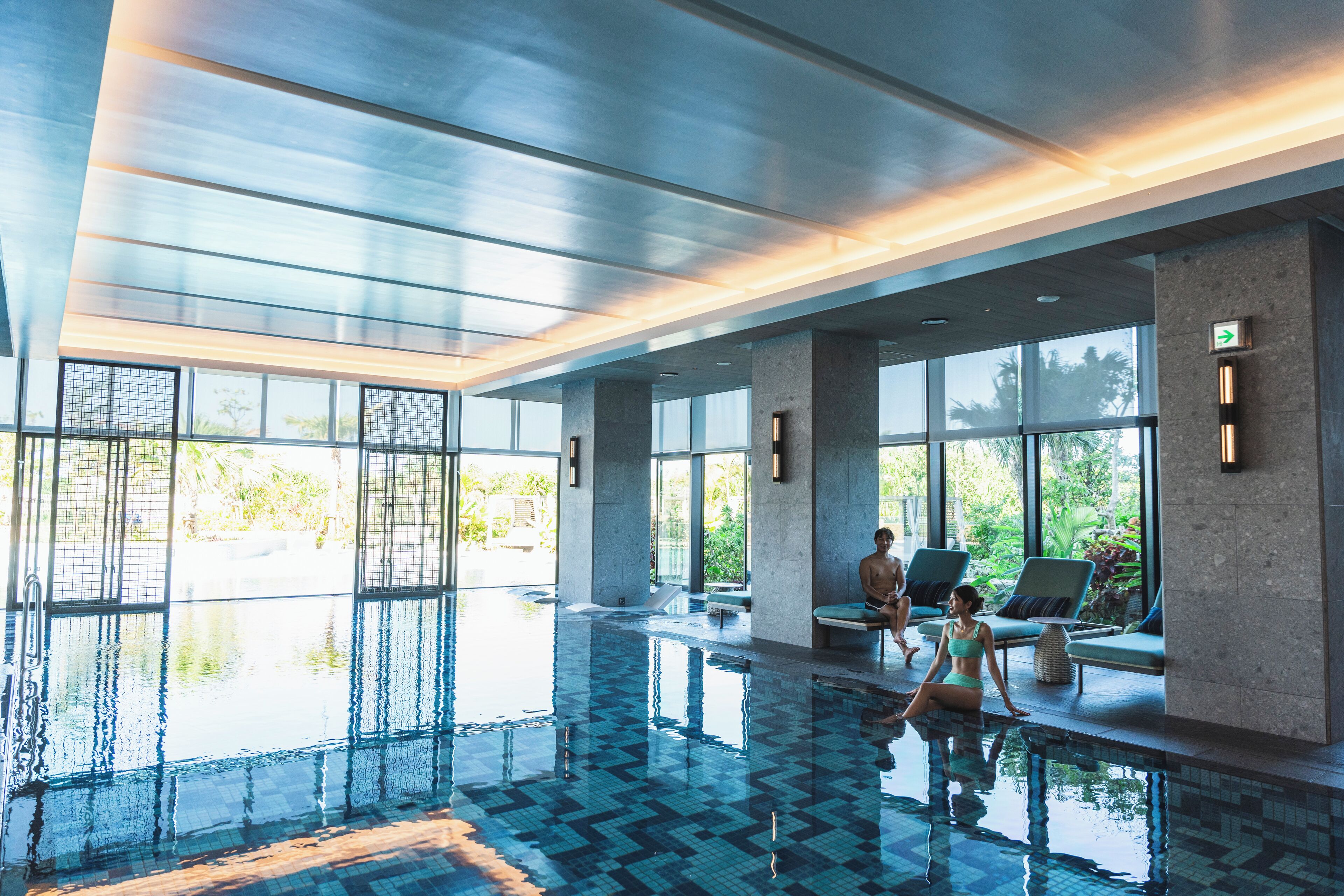 A modern indoor swimming pool with clear glass walls, large windows, and a tiled floor.