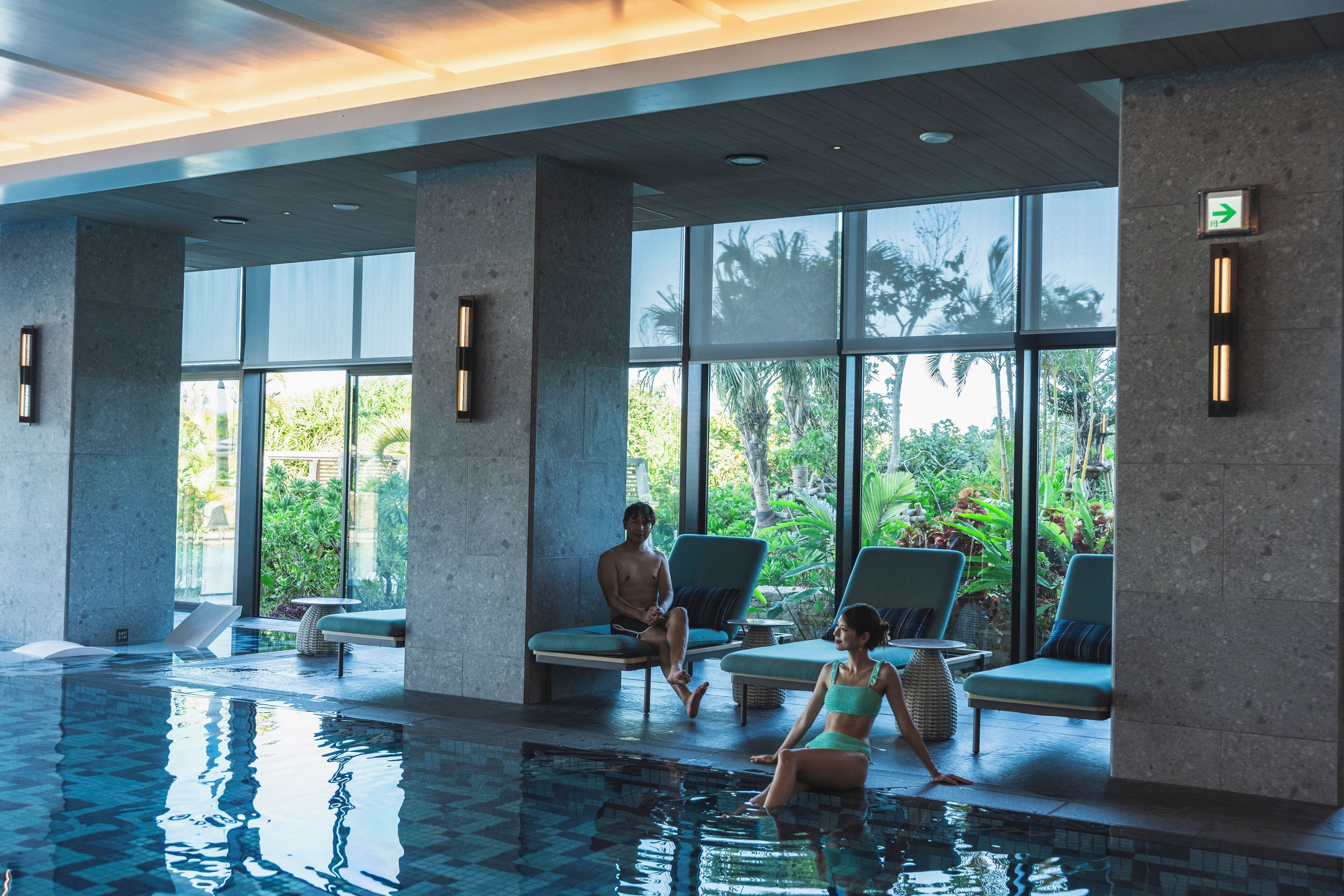 A swimming pool area with lounge chairs and a view of greenery outside.