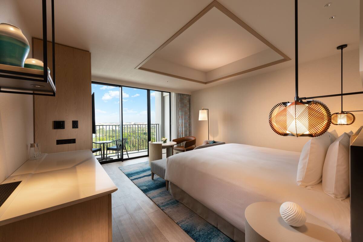Una habitación de hotel moderna con una cama grande, un escritorio, un balcón con vistas y una lámpara colgante.