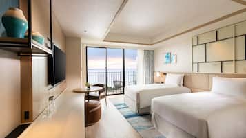 Quarto de hotel com duas camas, televisão, área de refeições e varanda com vista.