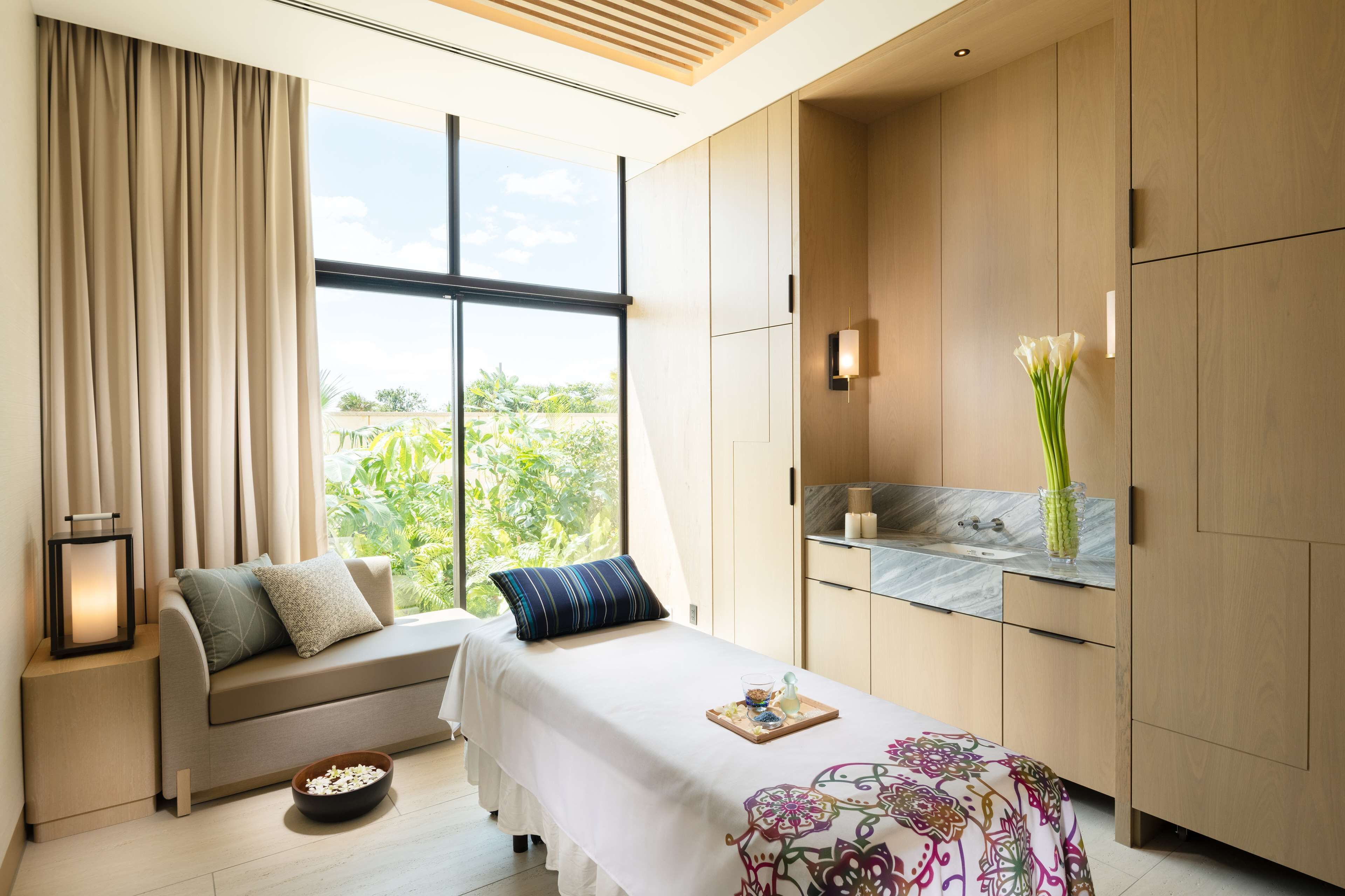 A modern bedroom with a sofa bed, a bedside table with a lamp, a tray with snacks, and a large window with curtains.