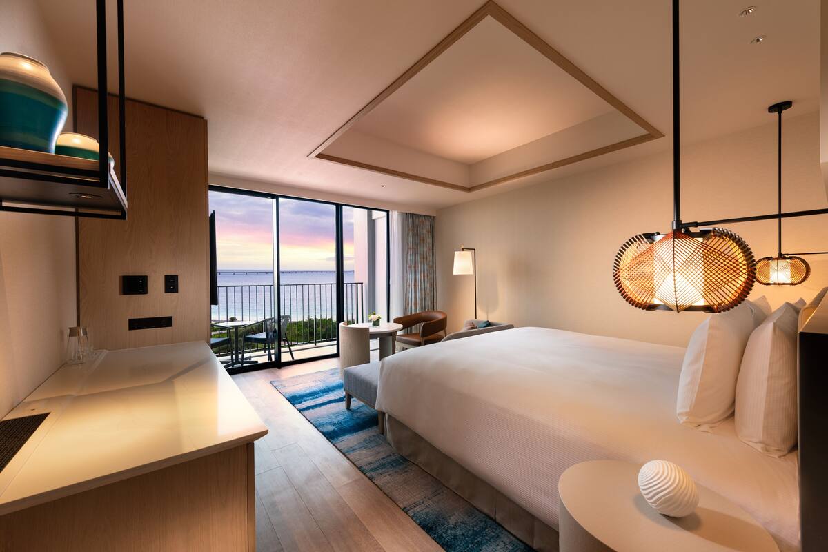 Una habitación de hotel moderna con una cama grande, un escritorio, un balcón con vistas y un comedor.