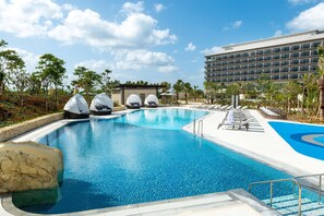 A hotel with a large swimming pool, lounge chairs, and palm trees. - Hilton Okinawa Miyako Island Resort (Miyakojima)