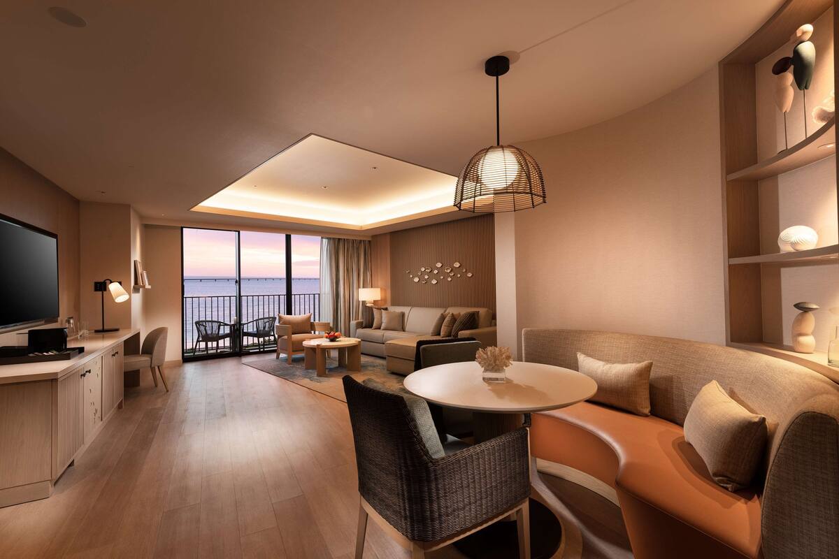 Una habitación de hotel moderna con balcón, comedor y sala de estar con sofá y sillones.