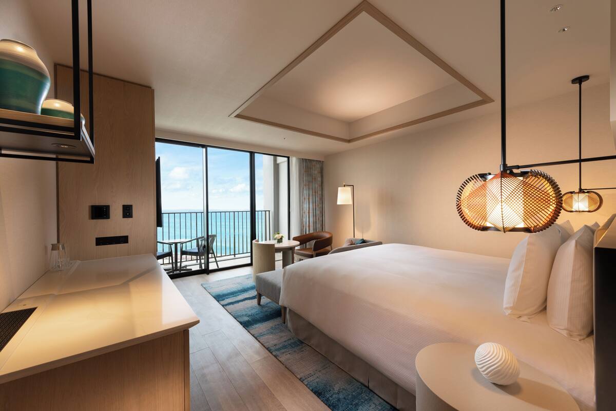 Habitación de hotel moderna con una cama grande, un escritorio, una silla y un balcón con vista al mar.