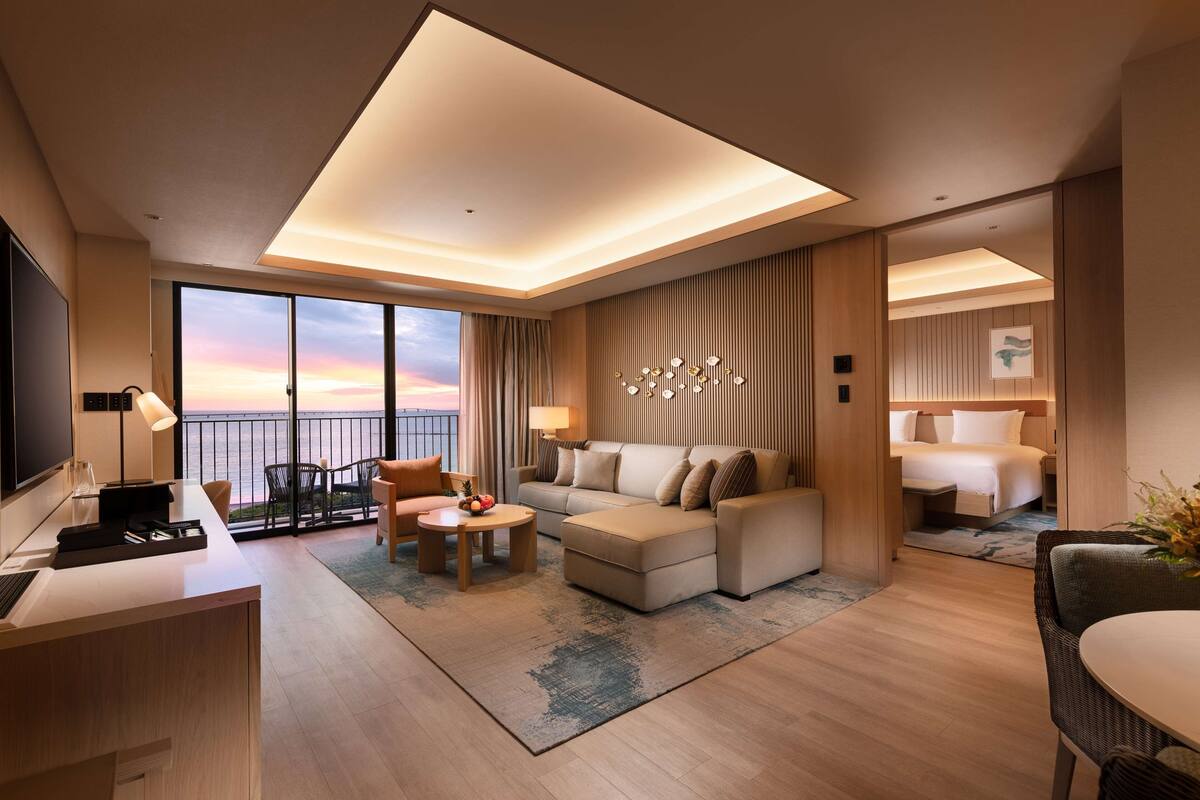 Una habitación de hotel moderna con un ventanal grande, un sofá, un escritorio y una cama.