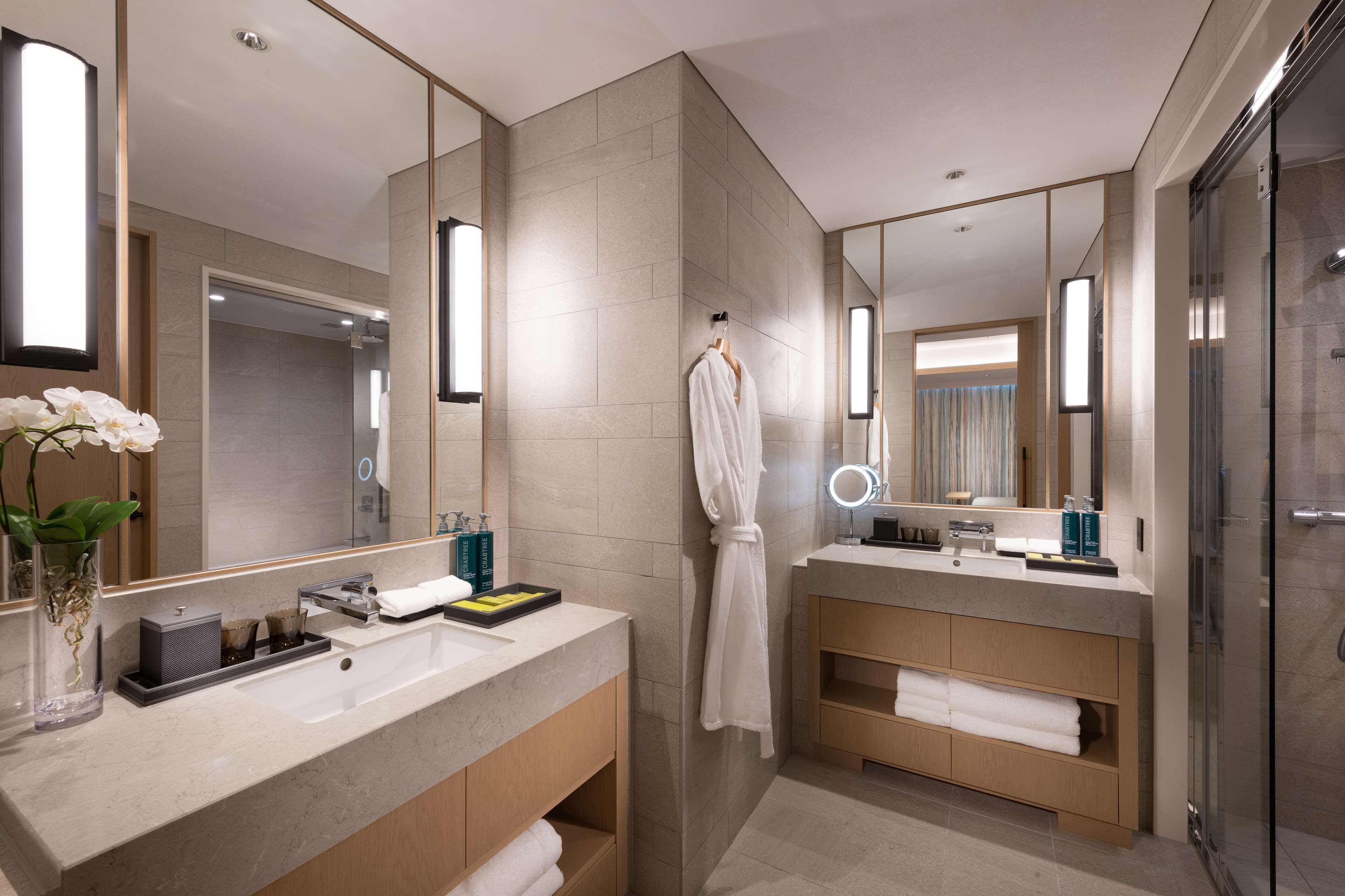A modern bathroom with dual sinks, a robe hanging, and a glass shower enclosure.