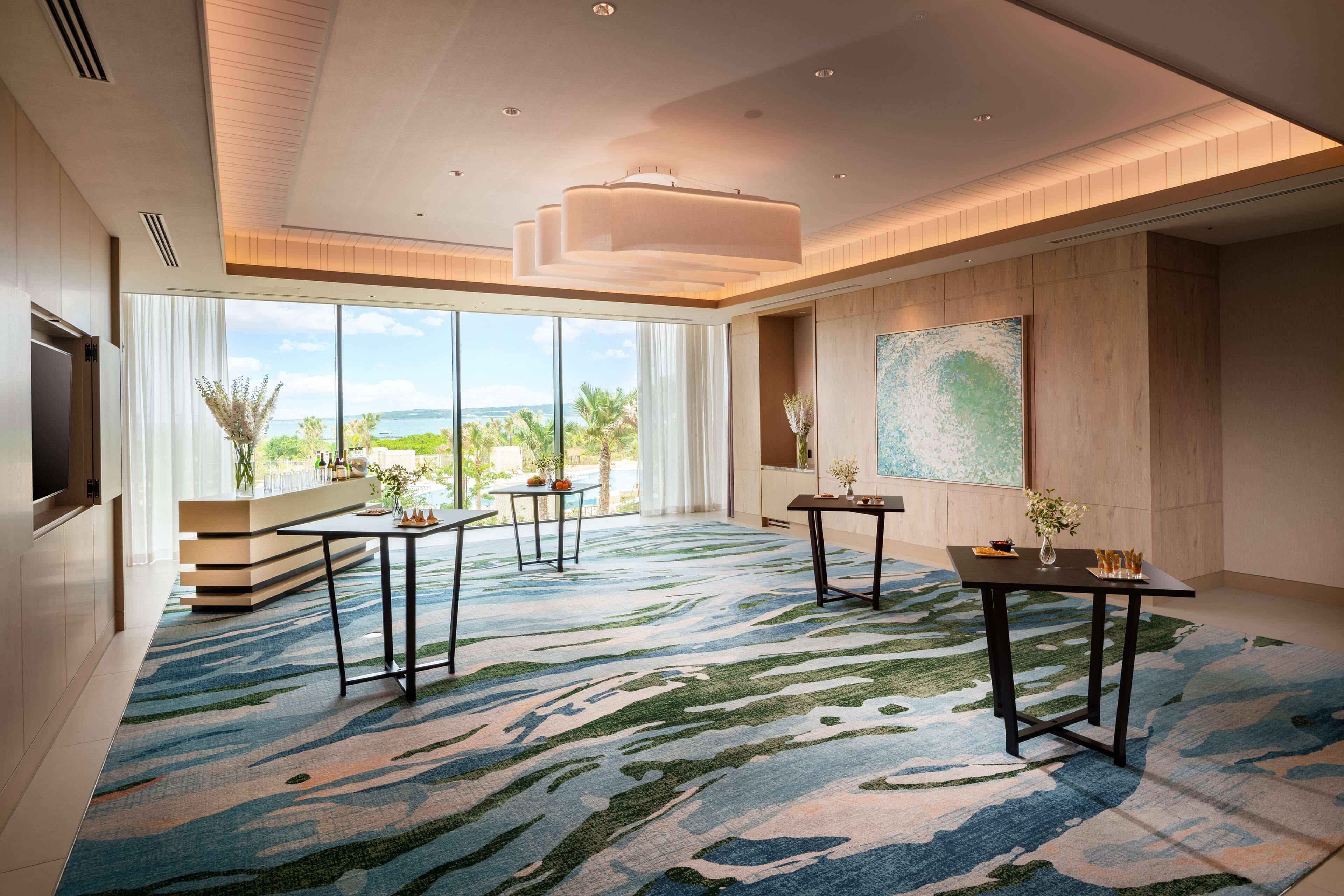 A spacious room with large windows, a modern chandelier, and a patterned carpet.
