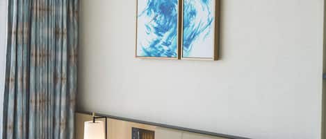 A hotel room with a bed, a wall-mounted lamp, and two framed artworks.