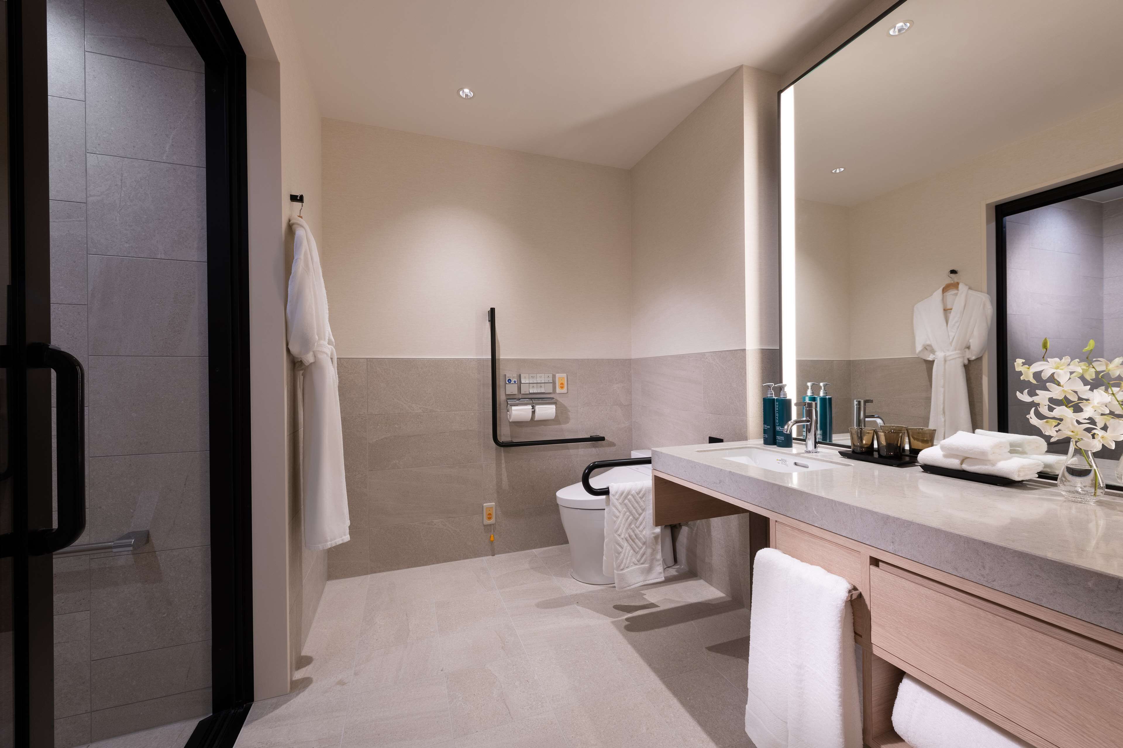 A modern bathroom with a large mirror, a shower area, and a vanity with toiletries.