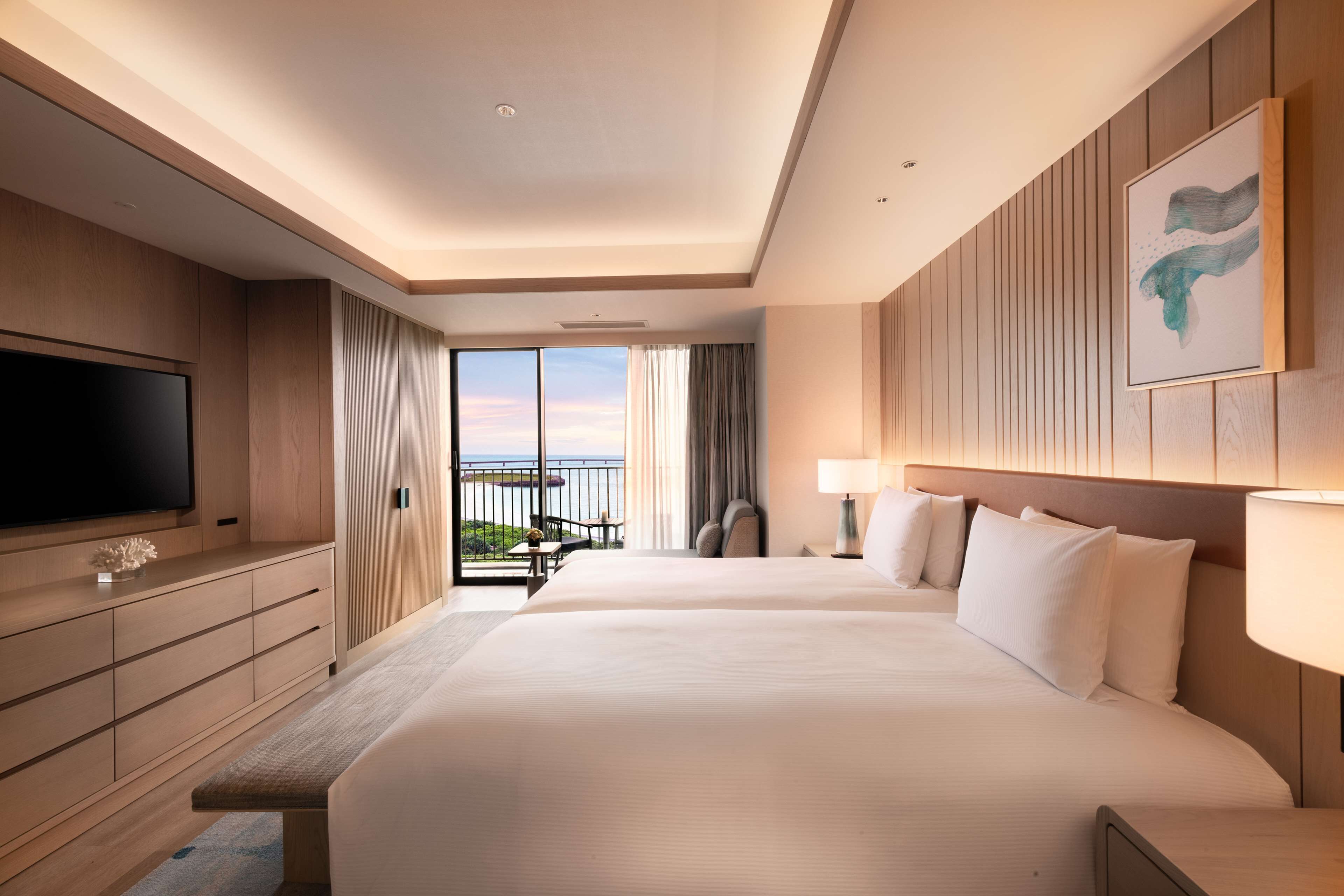 Habitación de hotel con una cama grande, televisión, escritorio y balcón con vistas.