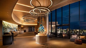A spacious lobby with modern lighting fixtures, a reception desk, and a seating area with a view of the cityscape. - Hilton Okinawa Miyako Island Resort (Miyakojima)