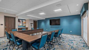 A conference room with a long table, blue chairs, a flat-screen TV, and a patterned carpet.