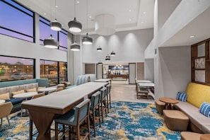 A modern hotel lobby with a long reception desk, seating areas, and large windows offering views of the outside.