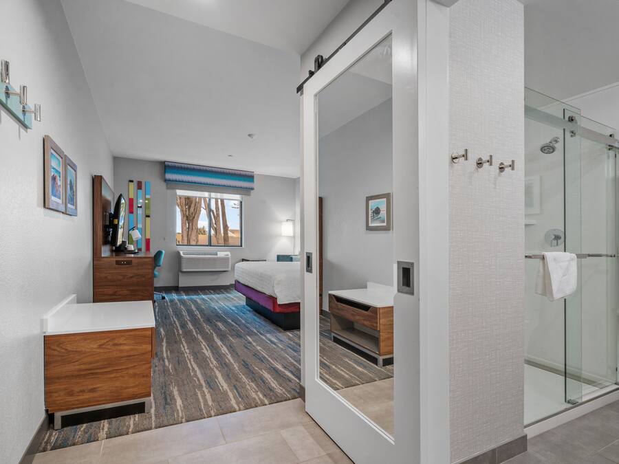 A modern hotel room with a large bed, a bathroom with a glass shower, and a view of the outdoors.