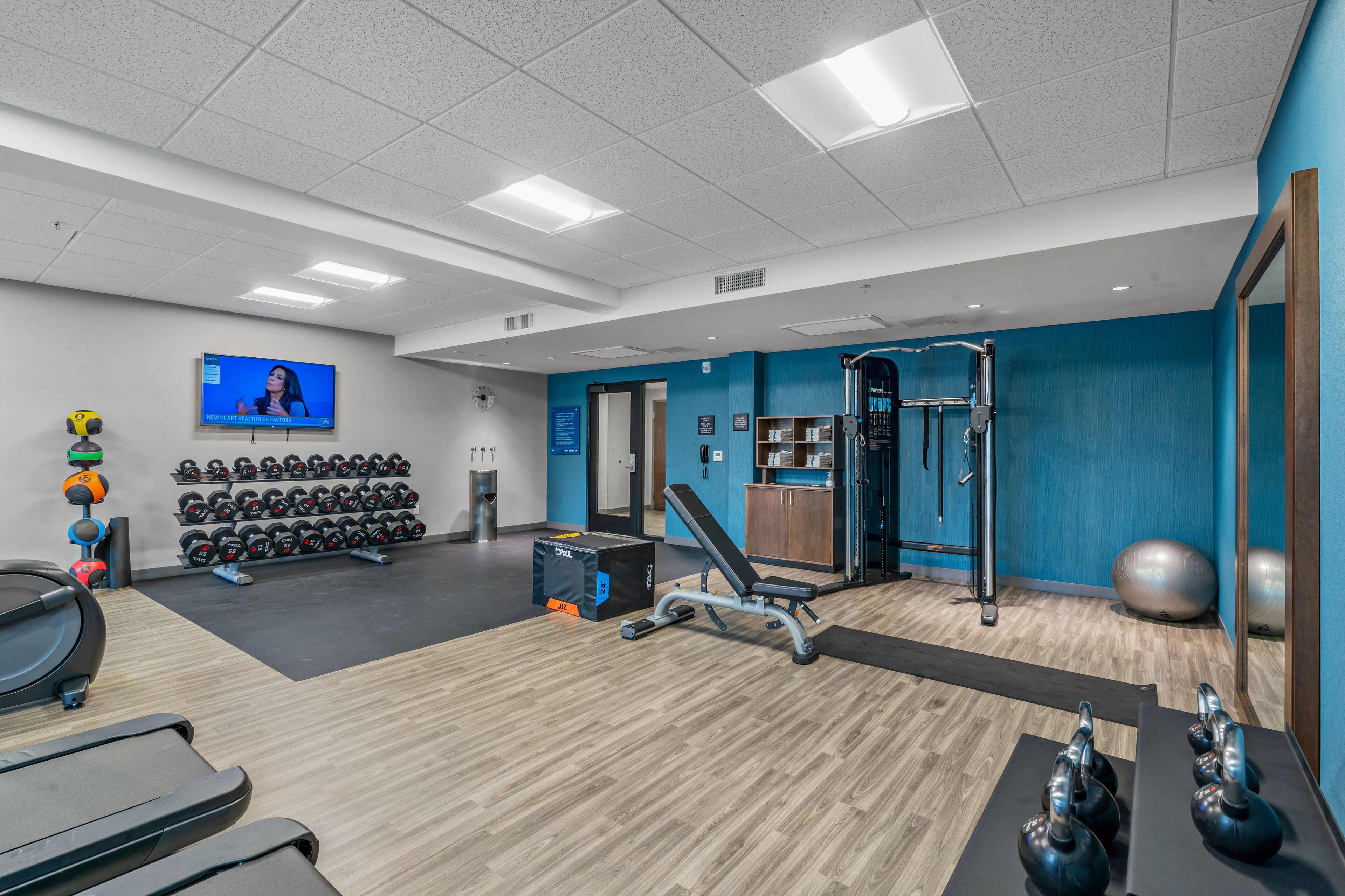 Une salle de sport équipée de matériel d’exercice, d’un téléviseur et d’un mur bleu.