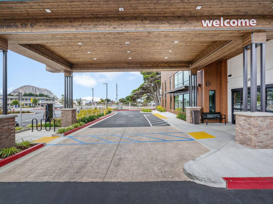 A modern building entrance with a 'welcome' sign, clear signage for parking, and a covered area with a wooden ceiling.
