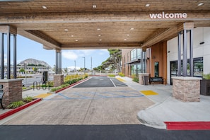 A modern building entrance with a 'welcome' sign, clear signage for parking, and a covered area with a wooden ceiling.
