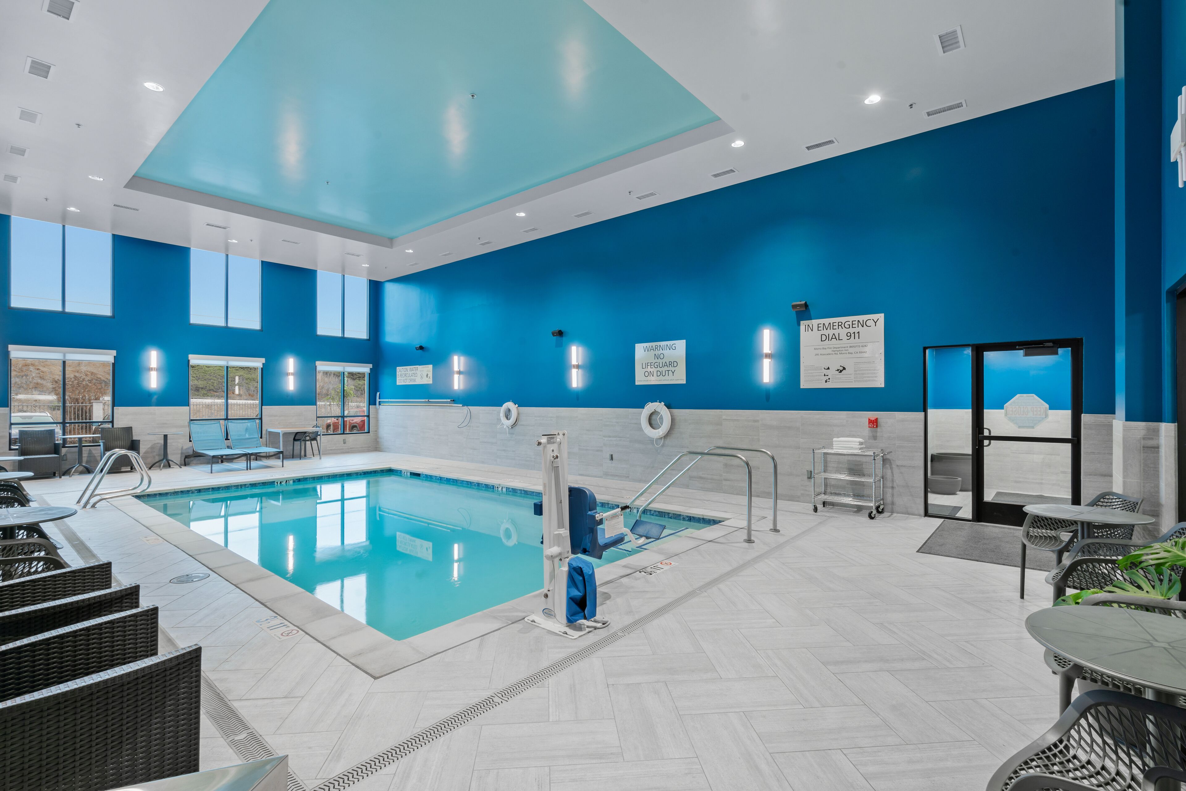 A modern indoor pool area with clear signage, a lifeguard station, and seating areas.