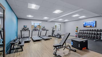 A gym with treadmills, elliptical machines, dumbbells, and a TV on the wall.