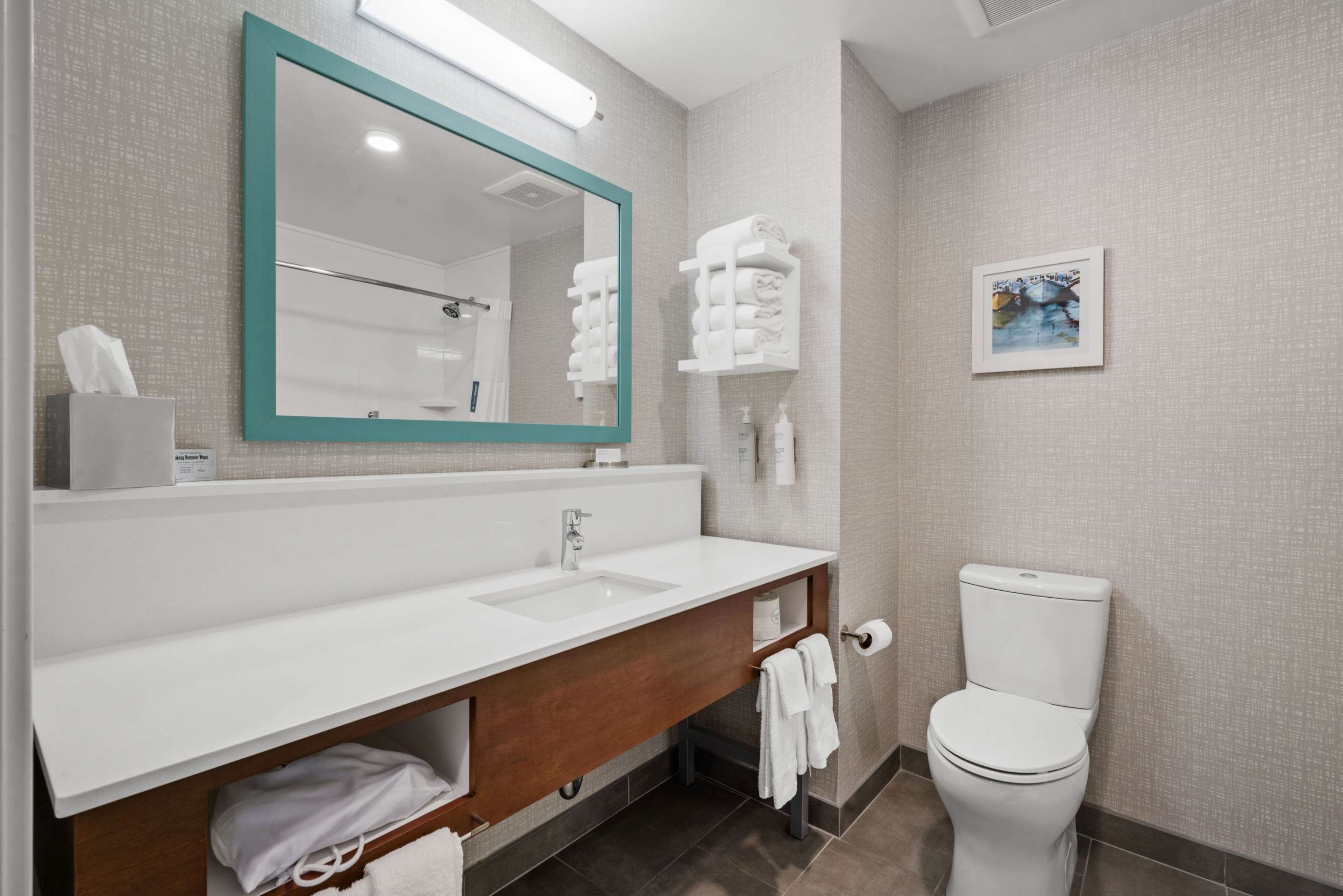 A modern bathroom with a white sink, a mirror with a teal frame, a toilet, and a towel rack.