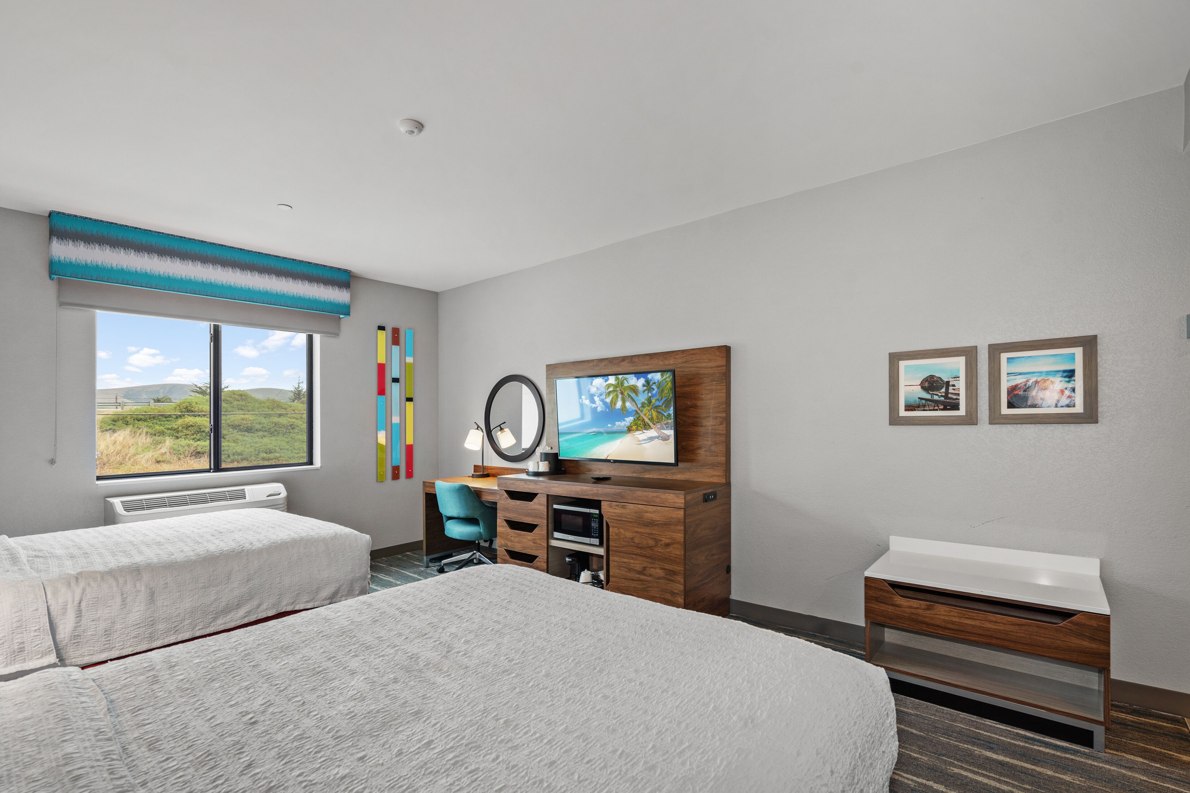 A hotel room with two beds, a desk with a computer, a TV, and a view of the outdoors.