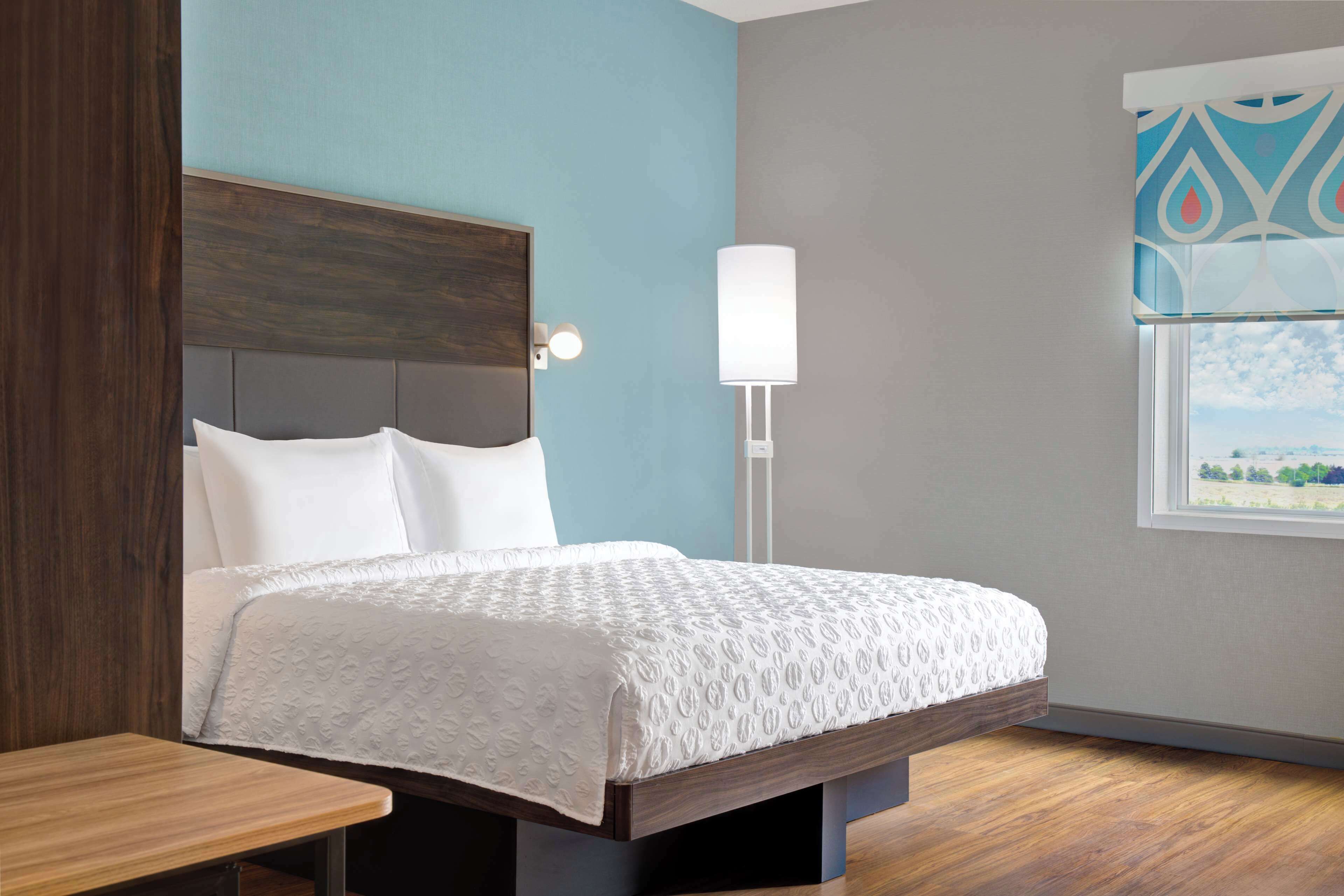 Una cama bien hecha con una colcha blanca, un cabecero de madera y una mesita de noche.