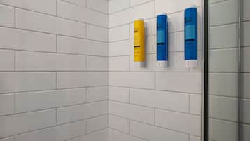 A bathroom with white tiled walls and three soap dispensers mounted on the wall.