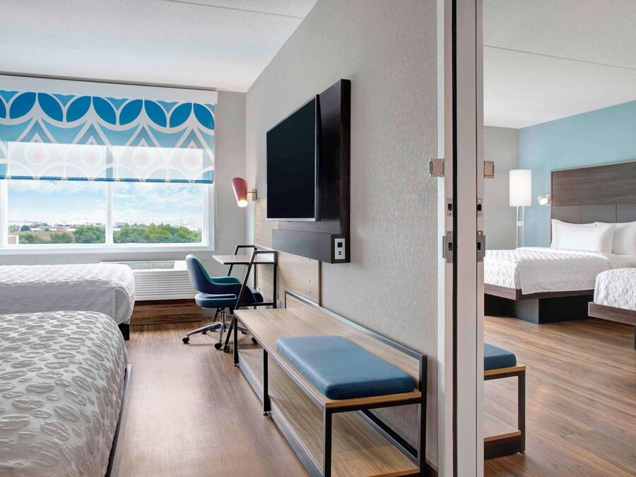 Habitación de hotel con dos camas, televisión, escritorio y vista a la ciudad.