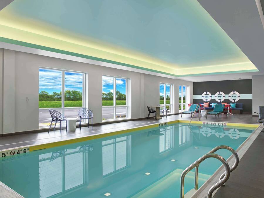 A swimming pool with clear blue water, surrounded by windows and chairs.