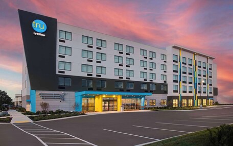 A modern hotel building with a prominent 'tru by Hilton' sign, a well-lit entrance, and a parking lot.
