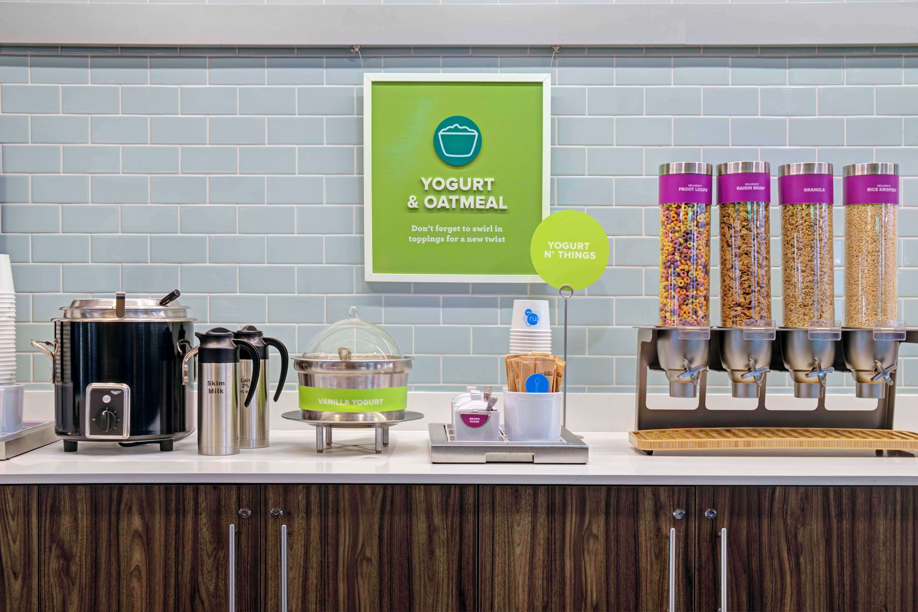 A yogurt and oatmeal station with dispensers, a coffee maker, and a sign encouraging creative toppings.