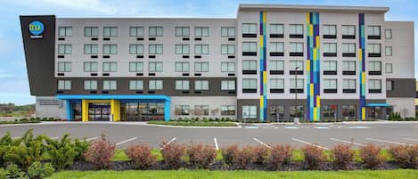 A modern hotel with a central entrance, multiple floors, and a parking lot.
