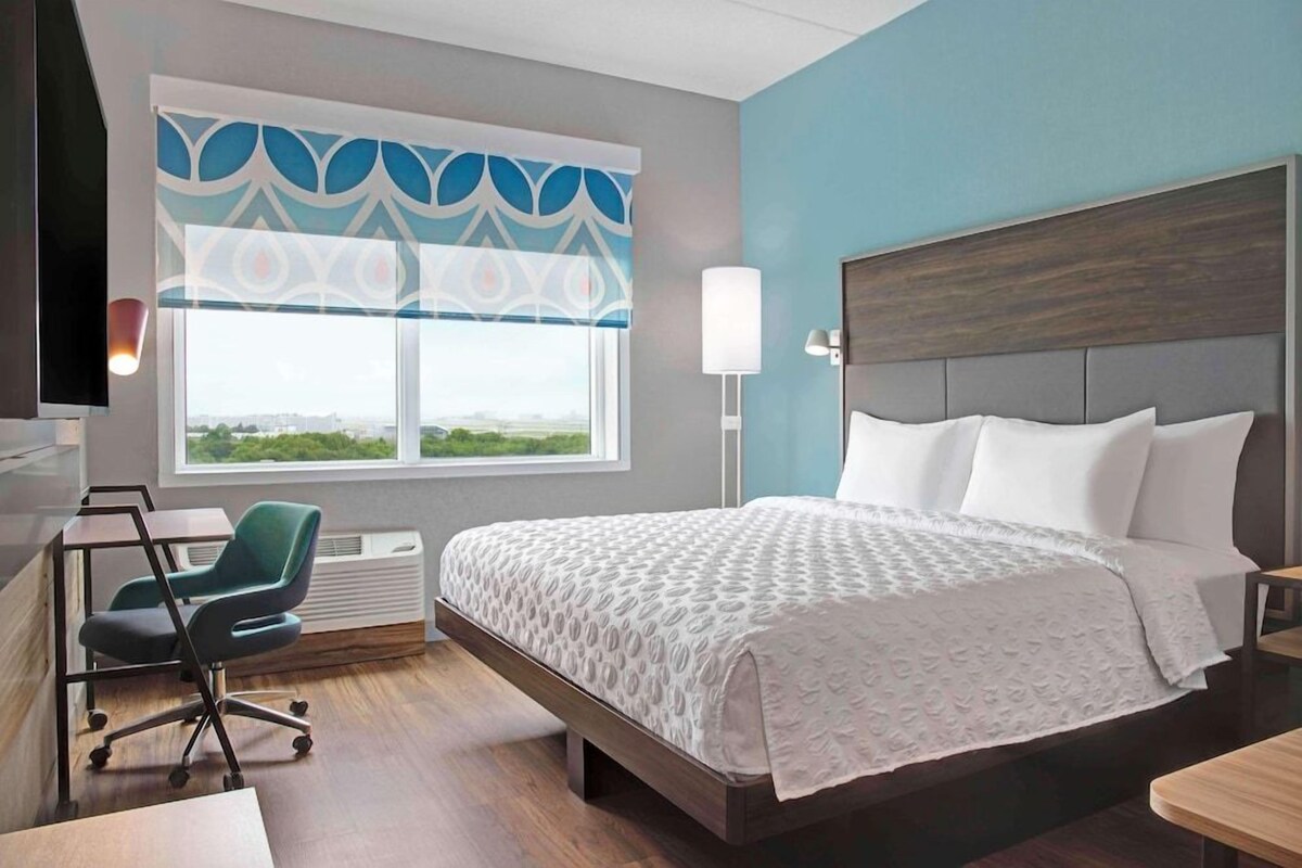 Une chambre d’hôtel équipée d’un lit, d’un bureau, d’une chaise, d’une fenêtre avec vue et d’un téléviseur fixé au mur.