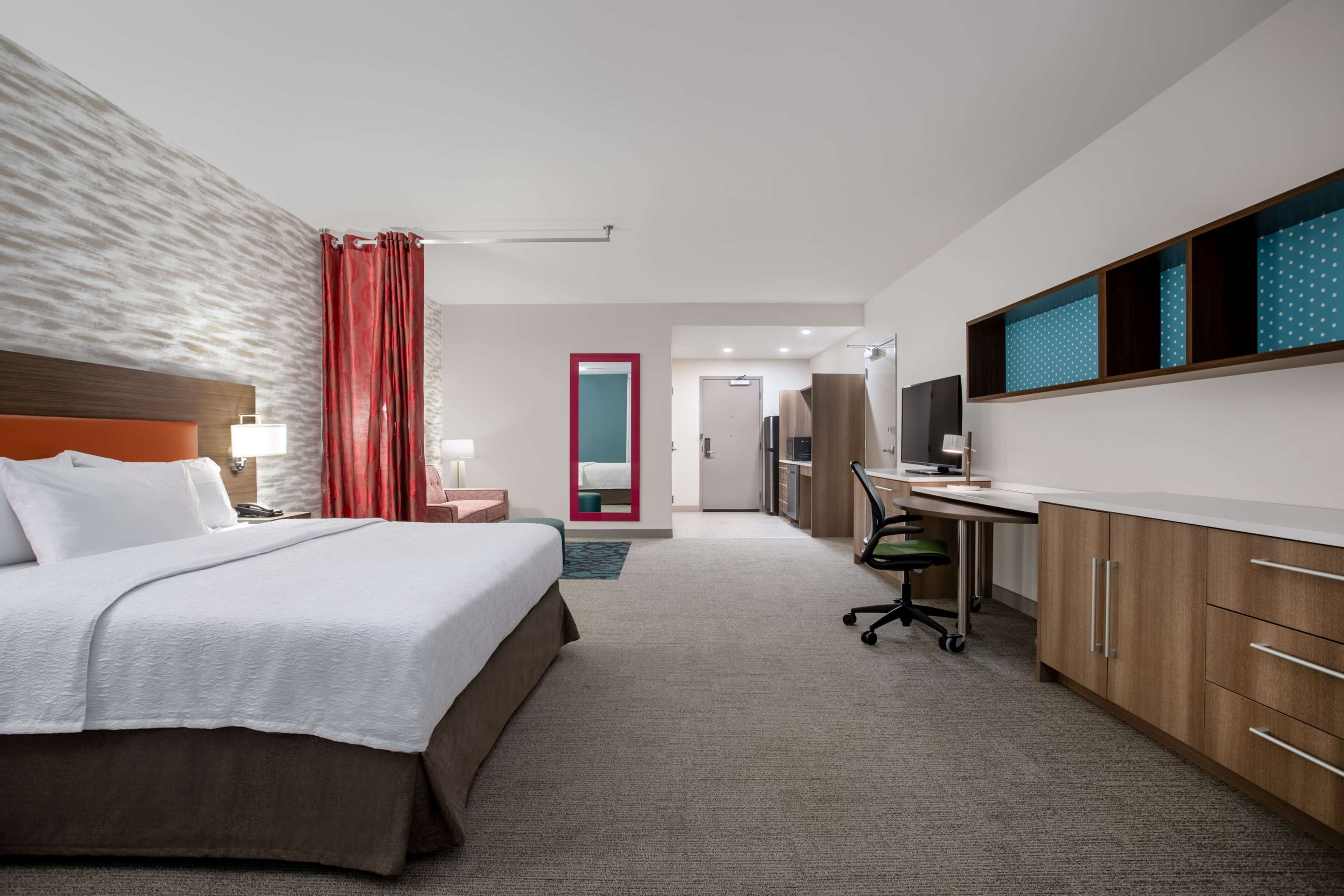 A hotel room with a large bed, a desk, a chair, and a TV.