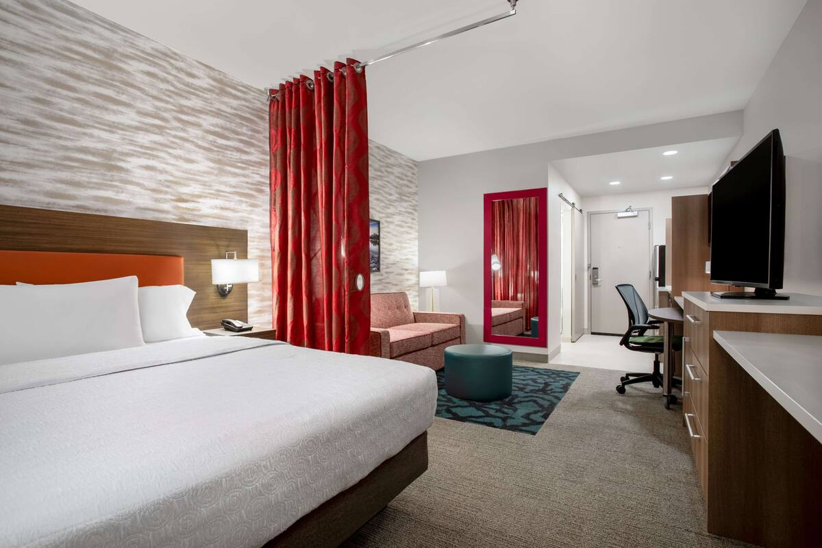 Una habitación de hotel con una cama grande, un escritorio con televisor, una silla, un sofá y un espejo.